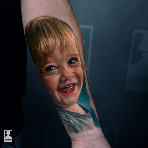 Kolorowy portret dziecka wykonany przez Marcina w realistycznym stylu. Autorski tatuaż w pełnym kolorze, z precyzyjnym odwzorowaniem emocji i detali, wykonany w INK-OGNITO Tattoo Rybnik.